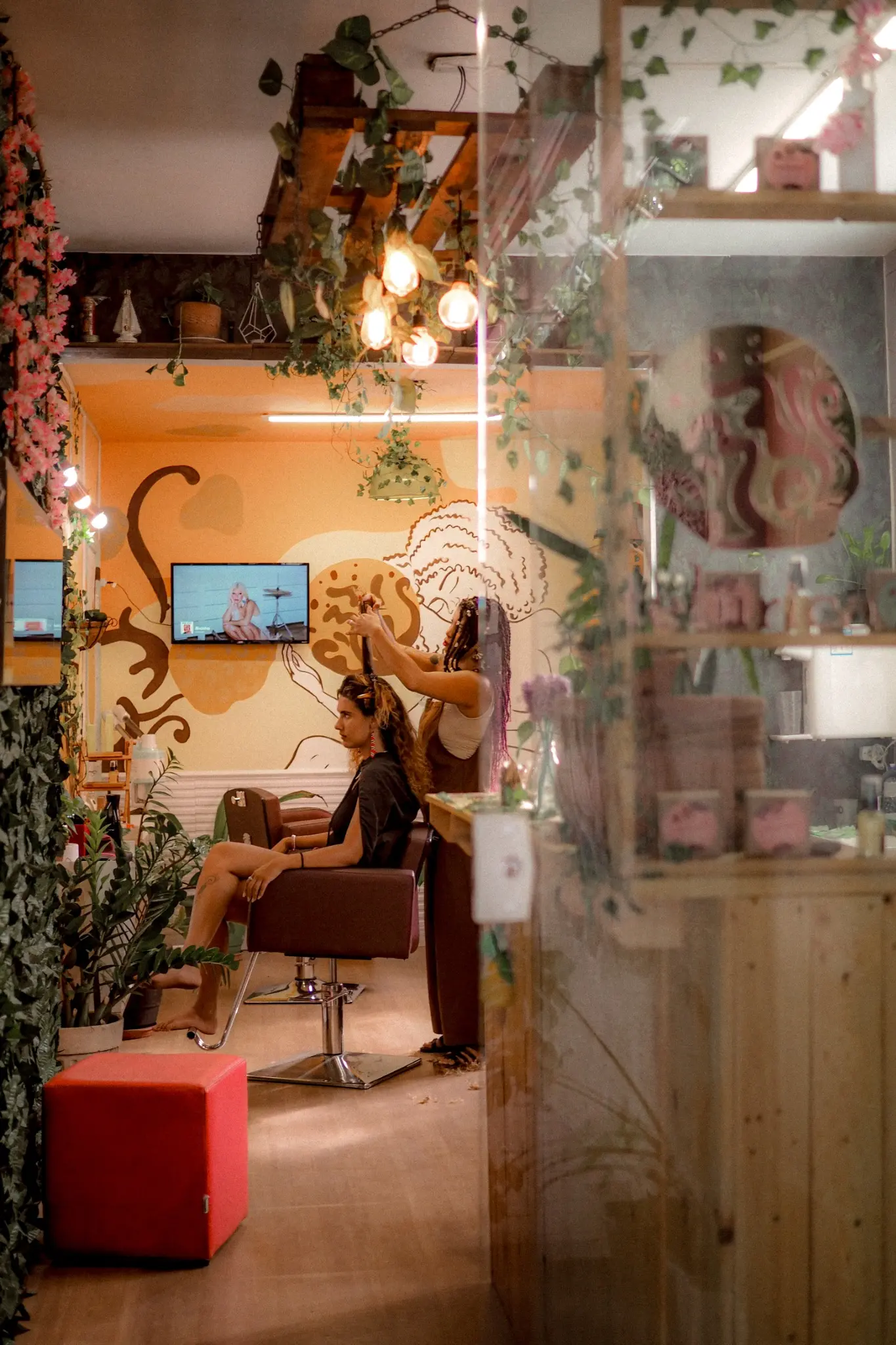 Interior do Espaço Telúrica visto através do vidro, com plantas, mural e atendimento acontecendo.